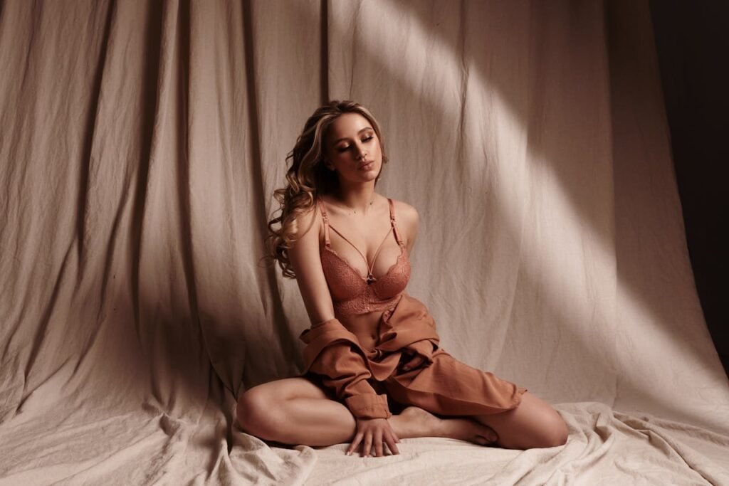 A woman posing gracefully in lingerie during a studio photoshoot with soft, muted tones.